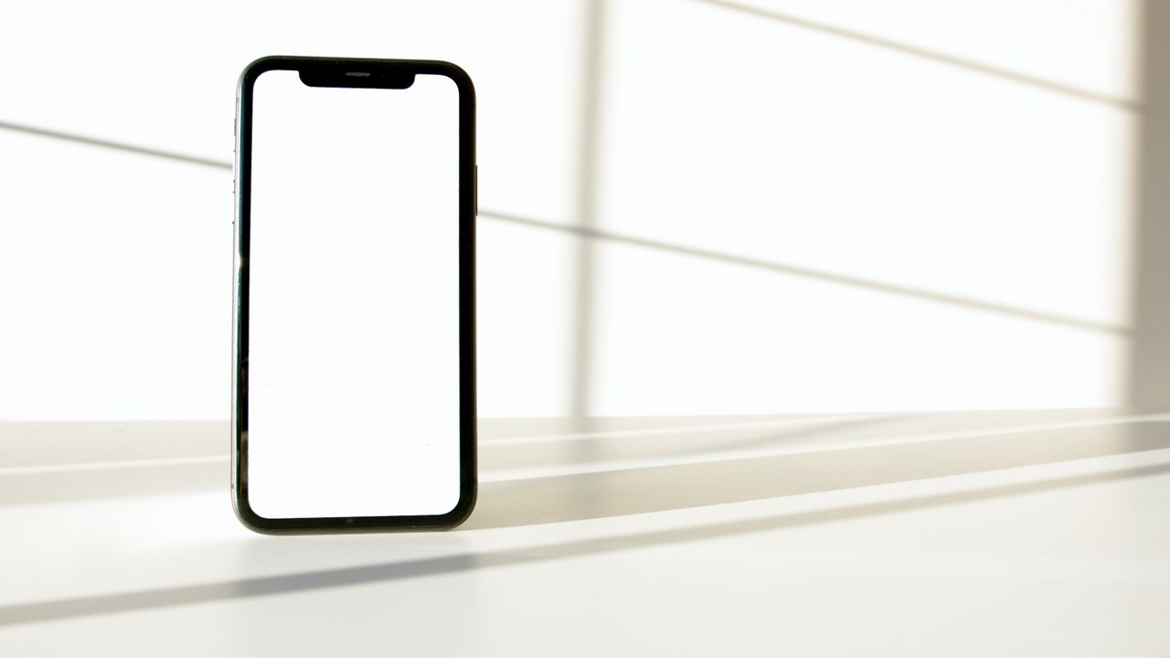Un smartphone élégant posé sur une surface blanche, avec un contraste marqué entre lumière et ombre.